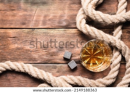 Whiskey in the drinking glass and mooring rope on the brown wooden flat lay table background with copy space.