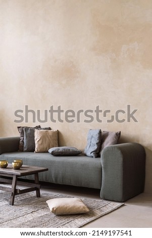 Vertical shot of green comfortable sofa with cushions stand against beige copy space wall in living room. Old rustic coffee table with tibetan singing bowls against sofa in cozy hygge apartment