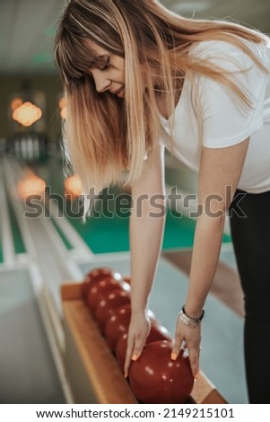 Young woman holding bowling ball and preparing to playing in the bowling club.