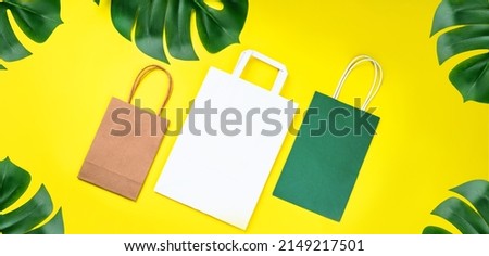 Recycled paper shopping bag with green leaves on yellow background. Zero waste, plastic-free concept. Environmental protection, sustainable living.food delivery concept