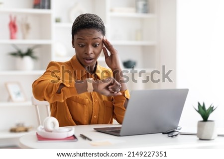 Attractive young african american business woman sitting at workdesk in front of laptop, working online, looking at watch and touching head, got late for business meeting, office interior, copy space Royalty-Free Stock Photo #2149227351