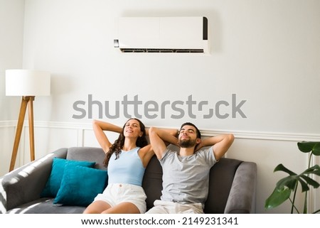 Latin attractive couple relaxing and resting on the couch with the air conditioner on during a hot summer  Royalty-Free Stock Photo #2149231341