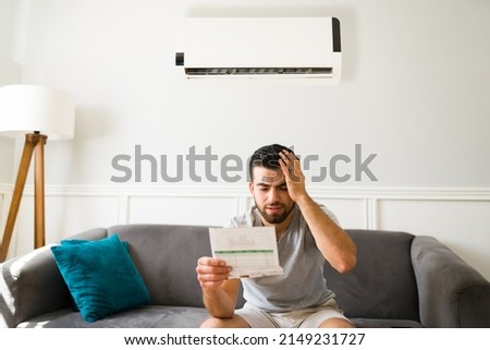 Expensive bills. Stressed latin man looking at the high electricity bill because of the air conditioning Royalty-Free Stock Photo #2149231727