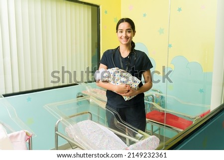 Beautiful happy nurse smiling while carrying a baby in the nursery room of the hospital  Royalty-Free Stock Photo #2149232361