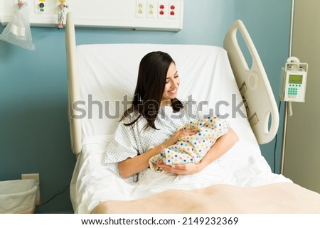 Cheerful new mother carrying and smiling to her newborn baby while resting on the hospital bed after giving birth Royalty-Free Stock Photo #2149232369