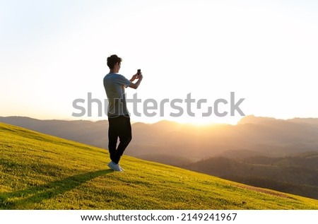 Man taking pictures with smartphone of sunset in mountains. Recording video with smartphone.