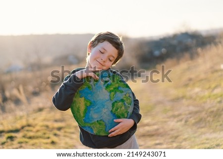 Protection and love of earth. Little boy holding planet in hands against green spring background. Earth day concept. Environmental Conservation