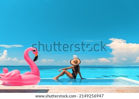 Travel on beach by pool on summer vacation in luxury resort. Woman relaxing in bikini by inflatable pink flamingo toy pool float on ocean turquoise background. Holiday travel destination concept. Royalty-Free Stock Photo #2149256947