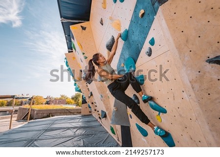 Asian climber woman climbing up outdoor bouldering wall at fitness gym. Fun active sport activity exercise outside Royalty-Free Stock Photo #2149257173