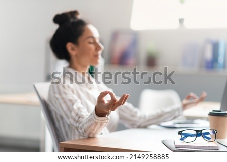 Workplace stress management. Female entrepreneur meditating and relaxing during stressful day, sitting at workplace in office interior. Focus on hand. Mental hygiene concept