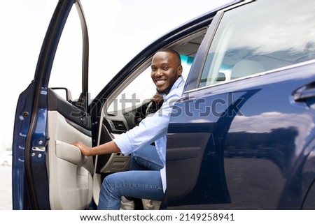 Test drive, Leasing, Buying, Rent Concept. Cheerful young African American guy going out or getting in the car, looking posing at camera. Happy black male open automobile door in the city outdoors Royalty-Free Stock Photo #2149258941