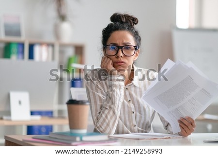 Tired female office worker looking at camera and holding documents, sitting at desk in office. Unhappy woman feeling stressed because of lot of paperwork Royalty-Free Stock Photo #2149258993