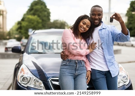 Happy Black Man Showing Keys Of Luxuy Automobile, Wife Embracing Her Husband, Young Family Using Auto Rental Service, Couple Buying New Car In Dealership Center Leaning On Vehicle, Posing At Camera Royalty-Free Stock Photo #2149258999
