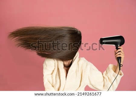 Woman drying her long hair with electric fan on a pink background. Royalty-Free Stock Photo #2149261677