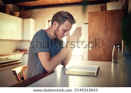 Going through his daily devotions. Shot of a devoted young man clasping his hands in prayer over an open Bible. Royalty-Free Stock Photo #2149263843