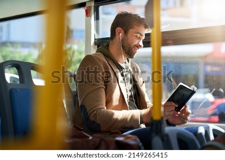 Checking out the best tourist spots. Cropped shot of a handsome young man reading a book during his morning bus commute. Royalty-Free Stock Photo #2149265415