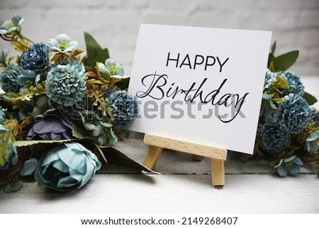 Happy Birthday text on wooden easel standing on white brick wall and wooden background