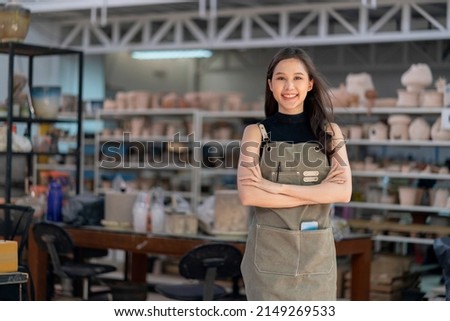 Asia female ceramist with apron hand confident chest in her workshop clay sculpture studio with positive smiling warm welcome ready to start new factory ceramic workshop with new collection of work