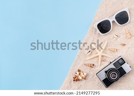 Top view with copy space of camera and sunglasses and starfish, shells with sand on blue background. Summer time concept.