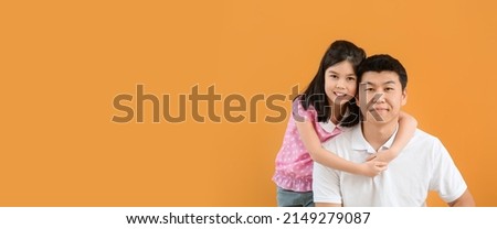 Happy Asian man and his little daughter on orange background with space for text