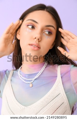 Fashionable woman with creative makeup and stylish jewelry looking aside on color background