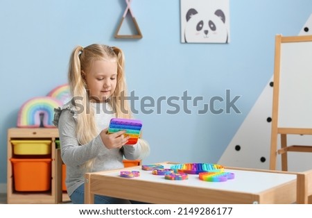 Pretty girl sitting at table and playing with multicolored pop it fidget toy in child room