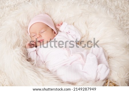Newborn Baby Girl sleeping over Fluffy White Blanket. Adorable One Month Child in Pink Bodysuit dreaming over Beige Furry Carpet. Cute New Born Kid relax