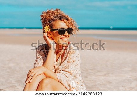 Portrait of happy tourist sitting and smiling at the beach with blue sky and ocean in background. Travel and tourism in summer holiday vacation. Female people with sunglasses on the sand Royalty-Free Stock Photo #2149288123