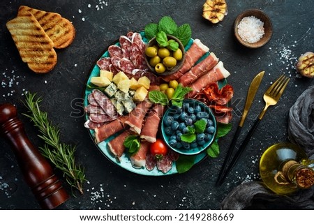 Italian snacks. Plate with cheese and ham, prosciutto, jamon salami, and snacks. On a black stone background. Royalty-Free Stock Photo #2149288669