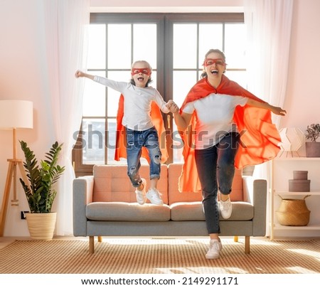 Mother and her child playing together. Girl and mom in Superhero costume. Mum and kid having fun. Family holiday and togetherness.