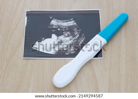 Pregnancy test showing a positive result and ultrasound picture of baby isolated on wooden background. Result of ultrasound picture or ultrasonography for pregnancy. Pregnancy care concept.