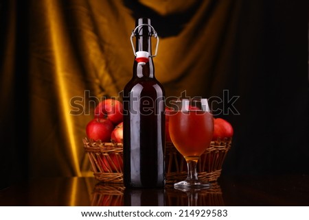 Bottle and glass of cider with ripe apples over a warm background