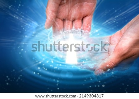 Cupped hands in water with glowing cross light. Sacrament of baptism religious theme concept. Royalty-Free Stock Photo #2149304817