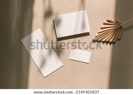 White paper sheets decorated with palm leaf on beige shadow background. Wedding invitation. Branding template,  newsletter concept. Top view, mock up, flat lay.