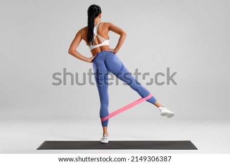 Fitness woman doing exercise for glutes with resistance band on gray background. Athletic girl working out
