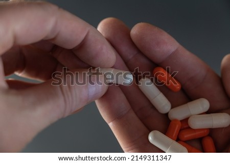 A man is holding white and orange medicine pills. The medicine lies in the open palm of an adult's hand. Health and Medicine.