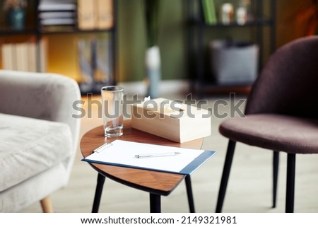 Clipboard with blank sheet, glass of water and napkin box on table in office of therapist Royalty-Free Stock Photo #2149321981