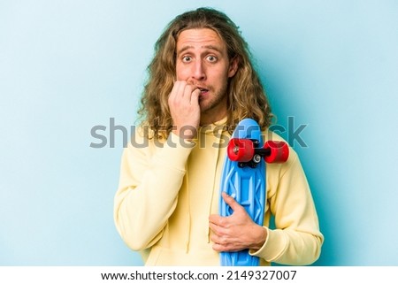 Young skater caucasian man isolated on blue background biting fingernails, nervous and very anxious.