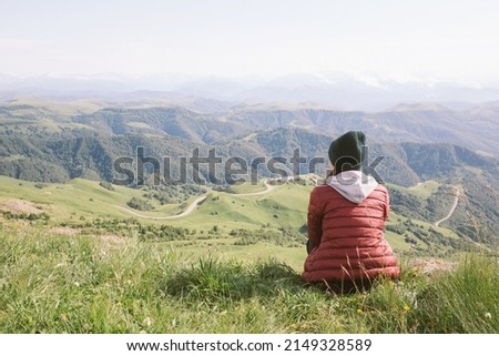 woman is sitting against background of mountains . travel, hiking, journey, outdoor recreation. Royalty-Free Stock Photo #2149328589
