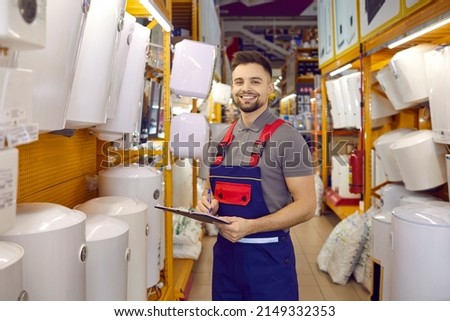 Smiling salesman or assistant in uniform work in building hypermarket with good restock. Portrait of happy male consultant check products in household or construction store. Retail concept. Royalty-Free Stock Photo #2149332353