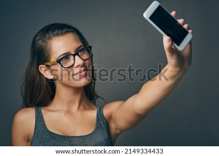 Your smile is the best filter you have. Studio shot of an attractive young woman taking a selfie against a grey background.
