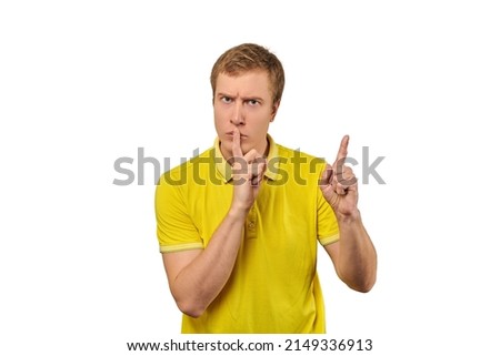 Funny male in yellow T-shirt asking to be quiet, silence gesture isolated on white background. Young man saying Shhh, keep quiet, please and making silence gesture, request for silence