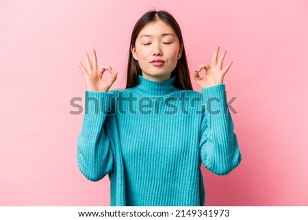 Young Chinese woman isolated on pink background relaxes after hard working day, she is performing yoga.
