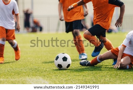 Group of multi-ethnic children playing soccer game. Young boys running after soccer ball on grass football field. Kids in orange and white jersey shirts. The player try to tackle a soccer ball Royalty-Free Stock Photo #2149341991