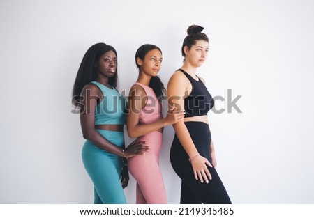 Side view of women in active tracksuits spending time together for sportive training in white gym studio, concept of aerobic class in pilates club - fit girls with different body types indoors