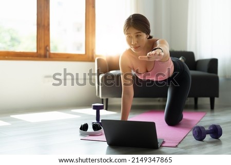 healthy sports asian woman in sportwear at home using laptop to share workout results in social media and doing abs exercises on fitness mat