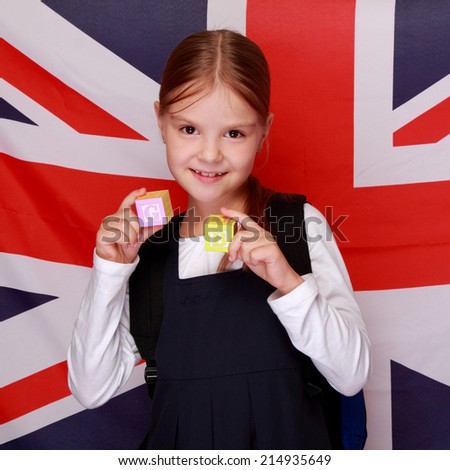 Studio image of a charming young schoolgirl holding cubes with letters of the alphabet on the background of the flag UK