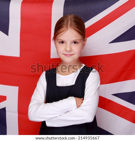 Happy smiling little girl in a school uniform stands on a background of the flag of Great Britain/British school girl on background of the flag of England