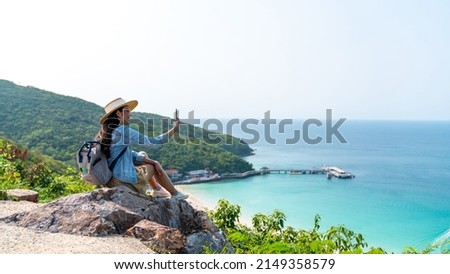 Young Asian woman traveler using mobile phone taking selfie while solo travel on tropical island mountain in summer sunny day. Cheerful female enjoy outdoor lifestyle in holiday beach vacation trip Royalty-Free Stock Photo #2149358579
