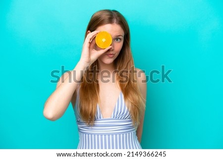 Young woman isolated on blue background in swimsuit and holding an orange